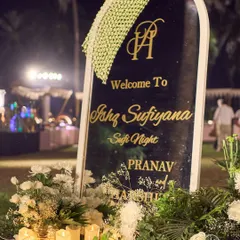 A personalized welcome sign for the 'Ishq Sufiyana' night, framed with lush white florals and glowing candles. The elegant script and mogra garland detail set a tone of bespoke luxury from the very beginning.