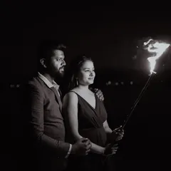 A dramatic black and white night portrait of a couple, their faces illuminated by the flame of a torch they hold together.