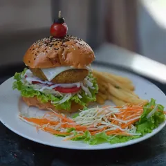 A classic veggie burger, made with a crisp patty, fresh lettuce, tomatoes, and a creamy sauce, served with a side of fries and salad. It's a satisfying and wholesome meal.