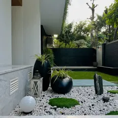 The same Zen garden, with a spherical light and a rustic lantern adding elements for evening ambiance. The contrast between the smooth white pebbles and the dark, rugged stones is a key feature.
