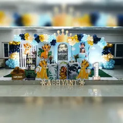 A complete Lion King themed first birthday setup featuring a custom sky-blue backdrop with a silver sequin archway. The decor includes multiple Simba character's, a large light-up number '1', and a balloon arch in royal blue, light blue, and gold.