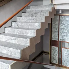 A detail of the marble steps and custom wooden handrail of the main staircase at the Bammi Residence. The design emphasizes clean lines and the natural beauty of the materials, creating a sense of understated luxury.