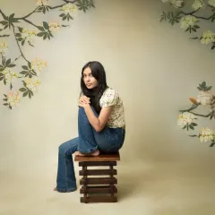 A relaxed, fine-art portrait. This image combines a casual, everyday outfit with the artistic touch of a painted floral backdrop, showing that authentic portraits can be both simple and beautiful.