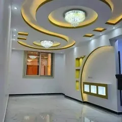 I specialize in creating complex, curved designs with gypsum. This living room features a flowing false ceiling with integrated chandeliers and cove lighting, which continues down into a custom-built wall unit with illuminated display niches.