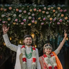 A triumphant moment for the newly married couple, raising their hands in celebration under a beautiful floral arch. This shot perfectly captures the joy of a North Indian wedding.