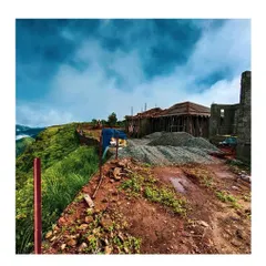 The construction site at Vagamon, showing raw materials stockpiled against a backdrop of rolling hills and a dramatic sky. This view illustrates the initial stages of transforming a challenging, sloped site into a thoughtfully designed recreational resort.