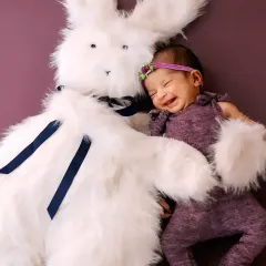 A heartwarming shot of a smiling newborn snuggling with a large, fluffy white bunny toy.