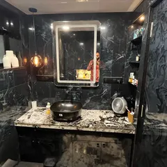 A luxurious bathroom design featuring black marble-patterned tiles on all walls. The space includes a custom vanity with a vessel sink, a backlit mirror, and accent pendant lighting for a dramatic effect.