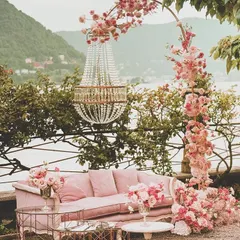 A romantic and picturesque seating area for two. The vintage pink sofa, floral arch, and hanging chandelier create a perfect photo spot, especially with a beautiful natural backdrop.