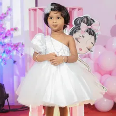 The perfect dress for a second birthday party. This custom white gown has a trendy one-shoulder design with a sparkling bodice and a multi-layered tulle skirt, ensuring the birthday girl stands out on her special day.