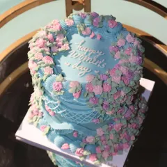 A stunning vintage-style cake for Women's Day. The beautiful blue frosting is adorned with a cascade of delicate pink and purple buttercream flowers, celebrating the grace and strength of women.