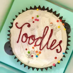 A close-up of one of our "Toodles" farewell cupcakes. You can see the smooth vanilla buttercream, the hand-piped message in red, and the mix of silver and rainbow sprinkles that add a bit of sparkle.