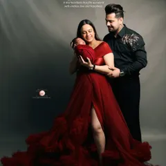 This portrait captures the elegance and joy of new parenthood. The mother's flowing red gown and the gentle way the parents hold their baby create a dramatic and beautiful family photograph.