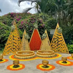 For this outdoor Haldi, we created a geometric backdrop with triangular panels of marigold and tuberose flowers. The setup includes two large urlis on a flower-strewn base, perfect for a garden ceremony.