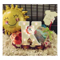 A sunny first birthday hamper for a baby. This gift includes a light-up initial 'K', a sun-shaped balloon, baby shoes, and a book.