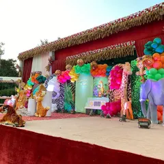 The main stage of this outdoor jungle party is filled with life-sized 3D props of elephants, giraffes, and tigers, set against animal-print backdrops and colorful balloon clusters.