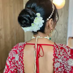 This elegant, low-slung bun is decorated with classic white carnations, a timeless choice for a bride. We focus on creating a smooth finish and a structure that holds throughout the wedding day.