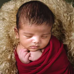 The same baby in a classic pose, with hands gently tucked under the chin. The lighting is soft and focused, creating a timeless portrait.