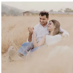 A quiet moment of connection in a field of golden grass. The soft, diffused light of the setting sun creates a warm, rustic, and incredibly romantic atmosphere for this pre-wedding portrait.
