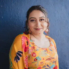A portrait against a bold blue wall, making the colors of her outfit and makeup pop. The look is fresh, modern, and perfect for a daytime Mehendi party.