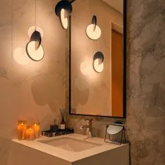 A sleek and modern bathroom with grey marble walls and a solid surface countertop. The sculptural pendant lights add an artistic touch and provide warm, flattering light.