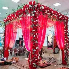 A stunning indoor wedding mandap completely covered in red fabric and dense red and white floral arrangements. This creates a rich and traditional space for the wedding ceremony.