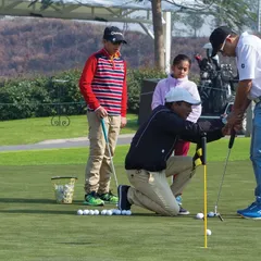 A coach provides hands-on instruction to junior golfers on the putting green, demonstrating our commitment to personalized lessons for every skill level.