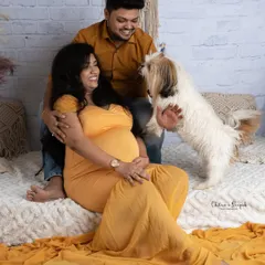 A candid and joyful maternity photo showing an expecting couple playing with their happy dog on a cozy, bohemian-style set in our studio.