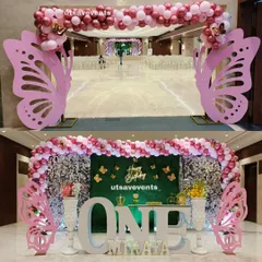 A grand butterfly-themed entrance arch and stage for a first birthday. The setup uses pink butterfly cutouts, a shimmer and grass wall backdrop, and a large 'ONE' sign for a stunning visual impact.