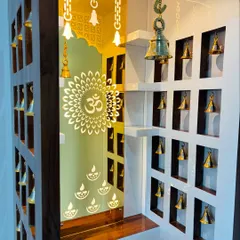 A close-up of the mandir's interior, showing the backlit 'Om' symbol and the small brass bells hanging in the side niches, creating a divine atmosphere.