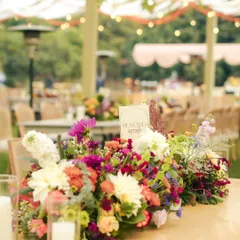 Let conversations bloom where the florals do. A close-up of a vibrant, wildflower-style centerpiece, complete with a custom-designed table name card, adding a personal touch to the wedding lunch.