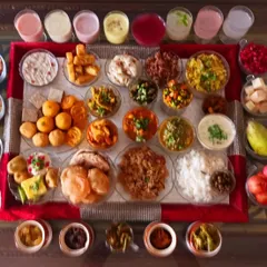 An overhead shot capturing the full expanse of the 56 Bhog spread. This includes a colourful array of drinks, sweets like jalebi and laddoos, savouries, pickles, and main courses, all made from plants.