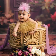A sweet and gentle smile from a baby girl during her studio photoshoot. The soft purple and floral elements create a delicate and warm portrait.