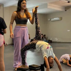 A student practices her bridge with a leg extension, using blocks for support. We use props to help dancers build strength and achieve advanced poses safely.