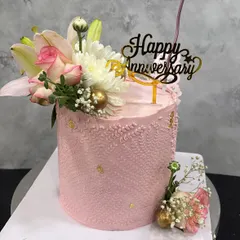 A blushing pink anniversary cake. This tall design is adorned with a beautiful arrangement of fresh lilies and roses, delicate piping, and flecks of gold leaf for a touch of magic.