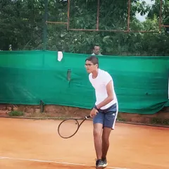 A young male player shows intense focus as he prepares to receive a serve in a tournament setting.