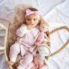 Celebrating six months of cuteness. This baby girl is dressed in pink, holding her dolls in a cozy basket.