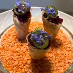 Miniature savory cones filled with a beetroot tartare and topped with pickled elements and edible flowers. A visually striking and flavorful start to a meal.