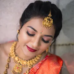 A detailed close-up of a classic bridal makeup look. The focus is on the flawless winged eyeliner, long lashes, and a bold, perfectly applied red lipstick, essential for a timeless South Indian bride.