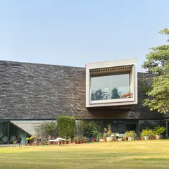 The Rhizome House, a farmhouse project completed in 2016. Here, a cantilevered volume clad in wooden shingles projects out from the main structure, framing a view of the landscape and demonstrating a blend of heavy concrete and lighter materials.