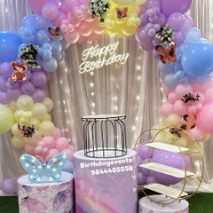 A pastel rainbow butterfly theme with a beautiful balloon arch and a "Happy Birthday" neon sign. The setup includes butterfly-themed plinths and decorative props for a magical photo opportunity.
