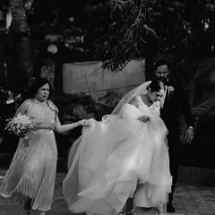 A candid black and white shot of the bride being helped with her dress by her mother and father, a moment of family support.