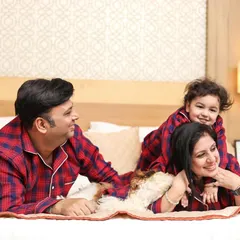 A playful family portrait on the bed, capturing genuine smiles and interaction between the parents, their child, and their furry friend.