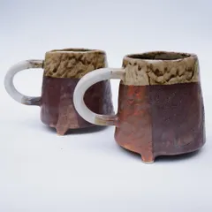 A pair of rustic, three-legged mugs. These are hand-built with a textured, multi-toned glaze and a simple, strong handle. They feel sturdy and comforting to hold.