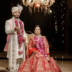 A classic wedding portrait that feels grand and timeless. I framed this shot to include the stunning chandelier, adding to the elegance of the moment. The couple is posed formally, showcasing the bride's magnificent red lehenga and the groom's coordinated white sherwani, capturing the complete look of their special day.