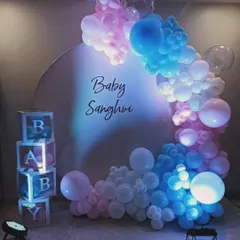 A creative gender reveal decoration using pink and blue lighting on a white balloon arch. This setup, with 'BABY' blocks and a simple backdrop, keeps the surprise until the final color is revealed.