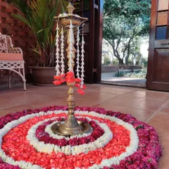 A beautiful floral rangoli made of red, pink, and white petals surrounds a traditional brass lamp (diya), creating a stunning and auspicious centerpiece for a Mehendi ceremony.