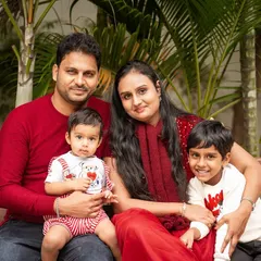 A beautiful family of four posing for an outdoor portrait. The coordinated red outfits create a warm and cohesive look against the natural green background.