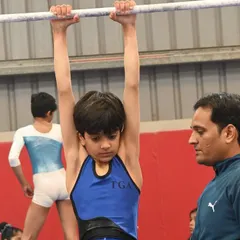 A coach provides close supervision as a young gymnast trains on the high bar. This focused attention is crucial for skill development and safety.
