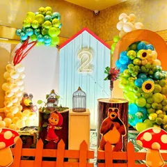 A delightful Masha and the Bear themed birthday setup. The decor features a house-like backdrop, character cutouts, toadstool props, and balloon arrangements that look like trees.